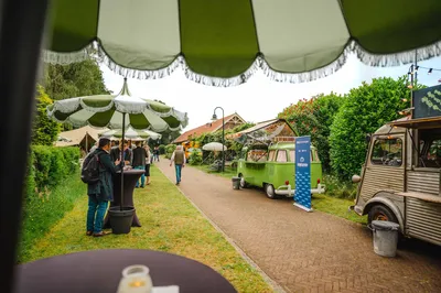 Bezoekers van een event bij verschillende foodtrucks en statafels in De Forttuin