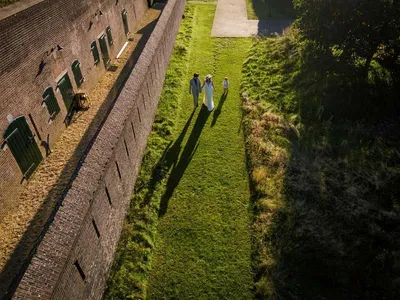 Dronefoto van bruidspaar dat langs de kazematten loopt
