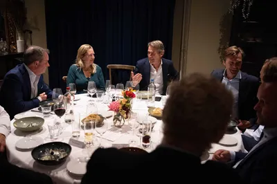 Personen aan een ronde met wit linnen gedekte tafel in De Loods